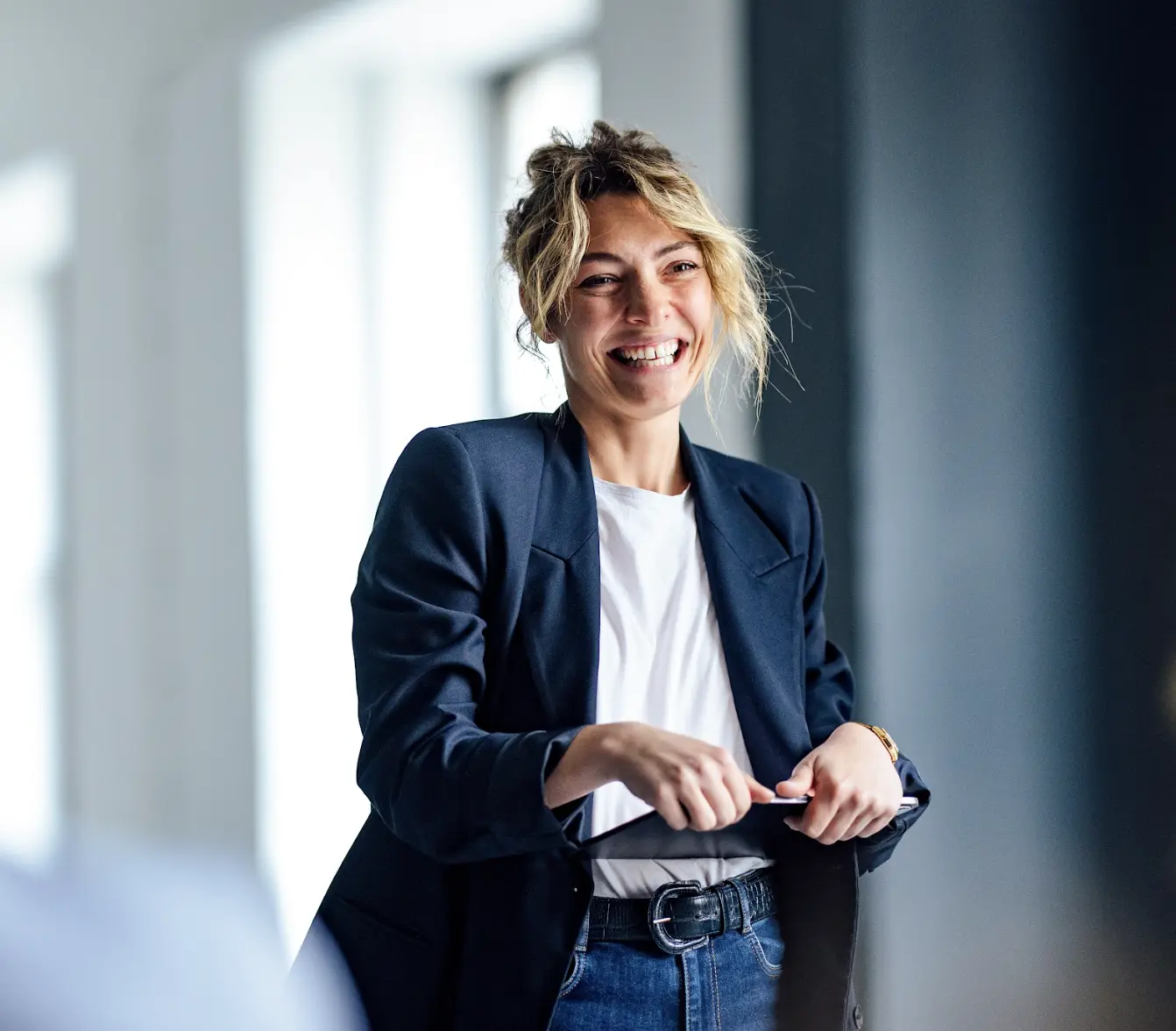 Confident businesswoman laughing during a casual meeting in a modern, sunlit office.
