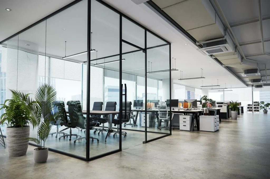 Modern open-concept office space with glass-walled meeting room, ergonomic chairs, and natural light from large windows.